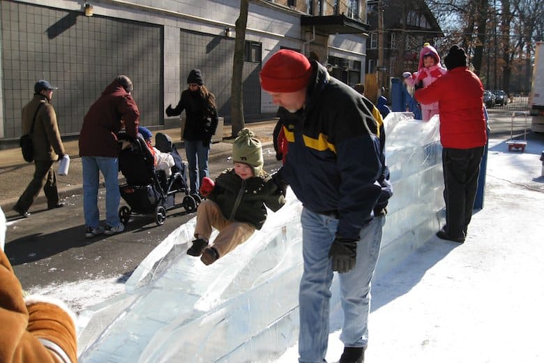 Child and Father play on an Ice Slide at a Winter Festival