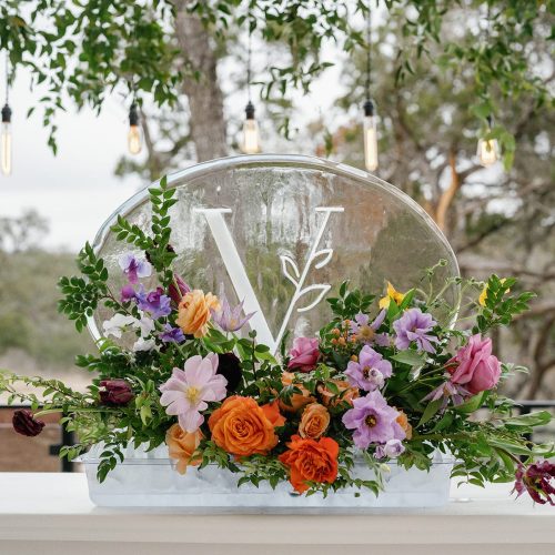 V carved into clear oval ice sculpture adorned with flowers