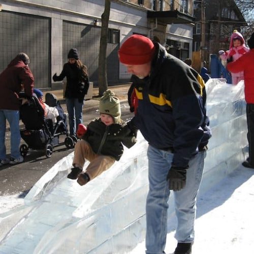 Child and Father play on an Ice Slide at a Winter Festival